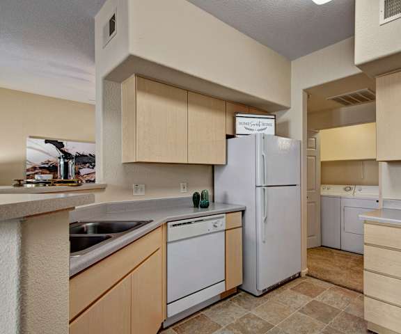 A cozy kitchen with white appliances, kitchen utensils, overhead lighting, light countertops with lots of room, and large wooden cabinets at Sonoma Landing Apartment Homes. 