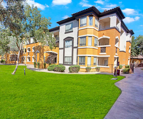 The beautiful yellow and white exterior of the apartments and the green space with grass, trees, and shrubs at Sonoma Landing Apartment Homes. 