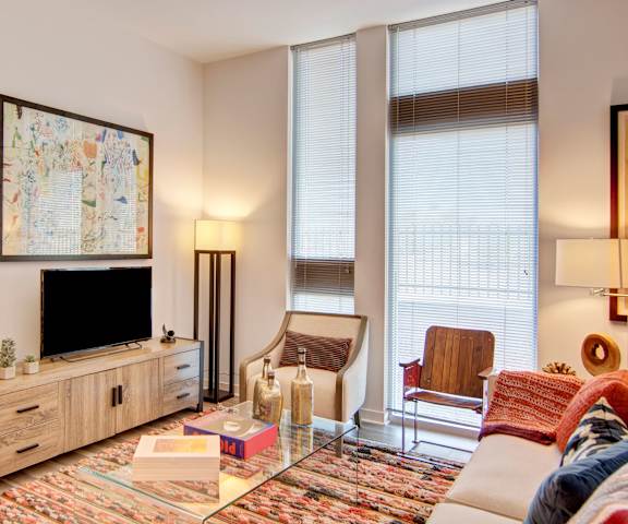 The spacious, white living room with a white couch, throw pillows, large windows, flowers in a vase, wall art, plush chairs, coffee table, decorations, large windows, and a TV at the Trend at 51 Apartment Homes. 