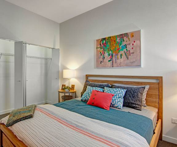 A spacious bedroom with a queen-size bed with a blue, white, and pink bedspread, a dresser, wall art, decorations, closet, and nightstands at the Trend at 51 Apartment Homes. 