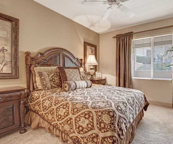A large bedroom with a queen-size bed, a plant, a dresser, decorations, window, and nightstands at Rancho Belago Apartments. 