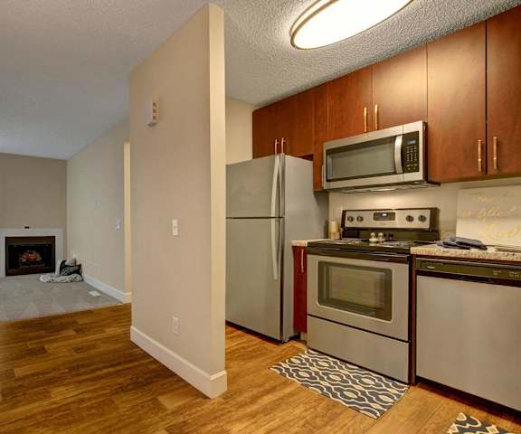 A kitchen with a refrigerator, microwave, oven, and dishwasher and a living room with a fireplace at 3600 Brentwood. 