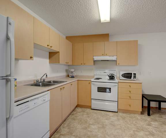 A kitchen with white appliances and wooden cabinets at Aspen Terrace. 
