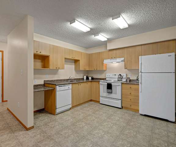An empty kitchen with white appliances and wooden cabinets at Birch Terrace Apartment Homes. 