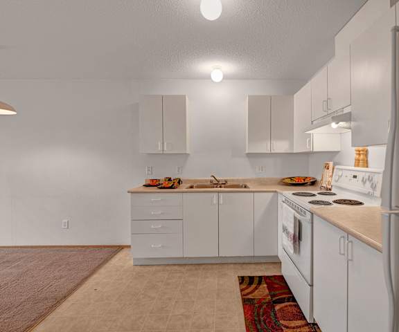A kitchen with white cabinets and appliances and a white refrigerator at Carrington Place Apartments. 