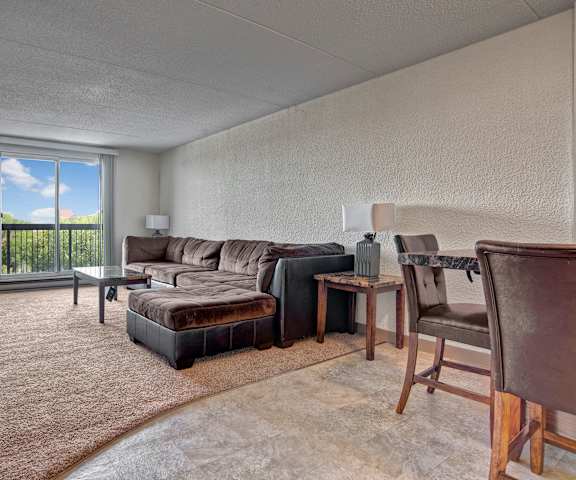 A living room with a couch, coffee table, tv, and dinner table with a door to the balcony at Centre Pointe Plaza. 
