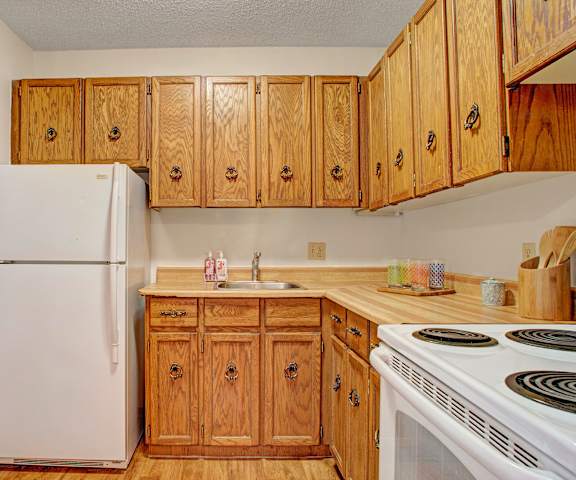 A cozy kitchen with white appliances, light counter with ample space, and spacious wooden cabinets at Madison Park Apartments. 