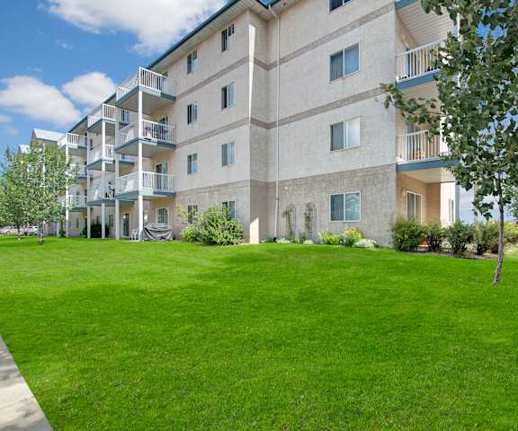 The exterior of the apartments and the green space with grass, trees, and shrubs at Manning Crossing Apartment Homes. 