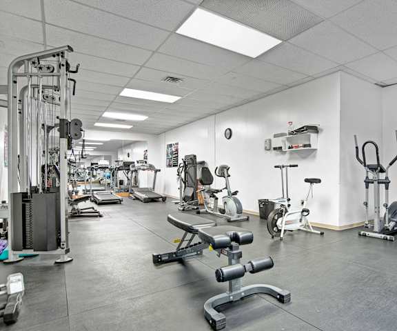 A gym with cardio machines, windows, TVs, and weights at Marquis Towers Apartments. 