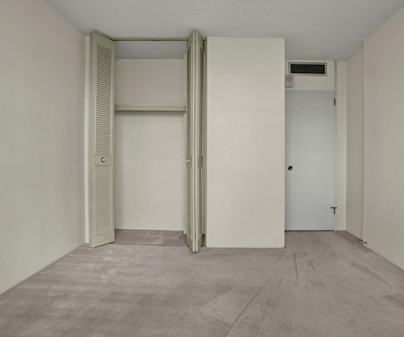 An empty carpeted bedroom with a closet at Marquis Towers Apartments. 