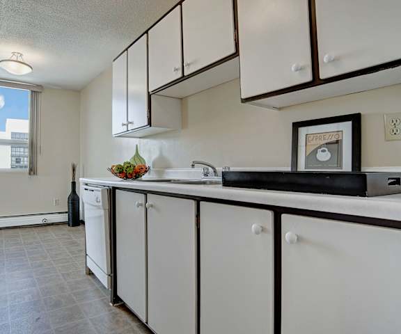 A cozy kitchen with white appliances, light counter with ample space, and spacious wooden cabinets at Marquis Towers Apartments. 