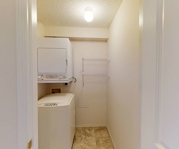 The laundry room with shelves, a washer, and a dryer at the Pointe at Applewood Apartment Homes. 