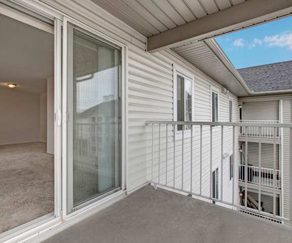  The concrete balcony with white metal railings looking into the empty carpeted living room at the Pointe at Applewood Apartment Homes. 