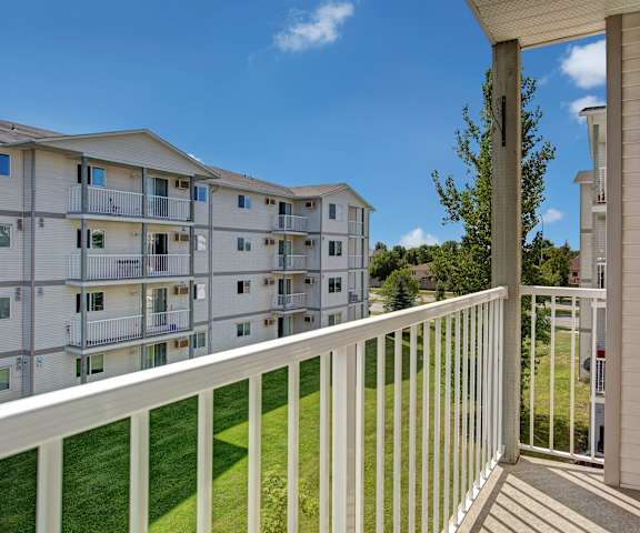 A white, wooden balcony with a gorgeous view of the other white buildings and the green space at Villagio Apartment Homes. 