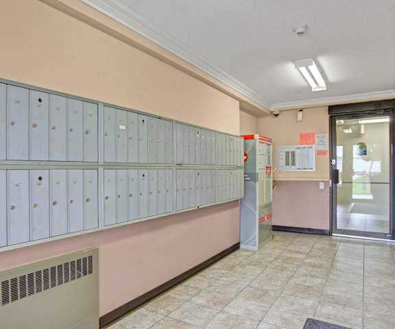 The mail room with rows of gray mailboxes lined up on a pink wall at Wellington Manor Apartment Homes. 
