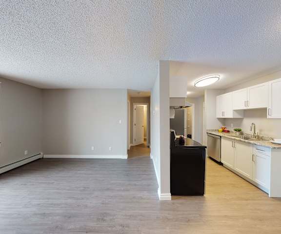 A view of the empty hardwood living room with a window and the kitchen with stainless steel appliances and wooden large cabinets at Wyndham Crossing Apartment Homes. 