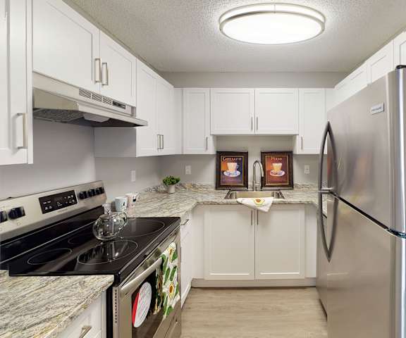 A kitchen with stainless steel appliances, marble countertops, and large white wooden cabinets at Wyndham Crossing Apartment Homes. 