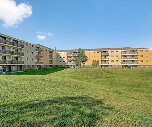 The exterior of the apartments and the green space with grass, trees, and shrubs at Wyndham Crossing Apartment Homes. 