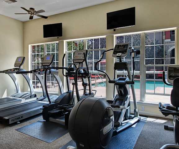 Camelback Pointe Cardio Equipment Facing Pool A gym with cardio machines, TVs, and a window view of a pool at Camelback Pointe Apartments.