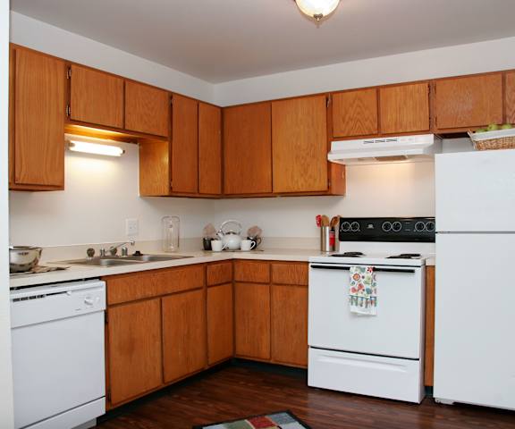 A kitchen with white appliances, light counter, and spacious wooden cabinets at Hyde Park North Apartments. 