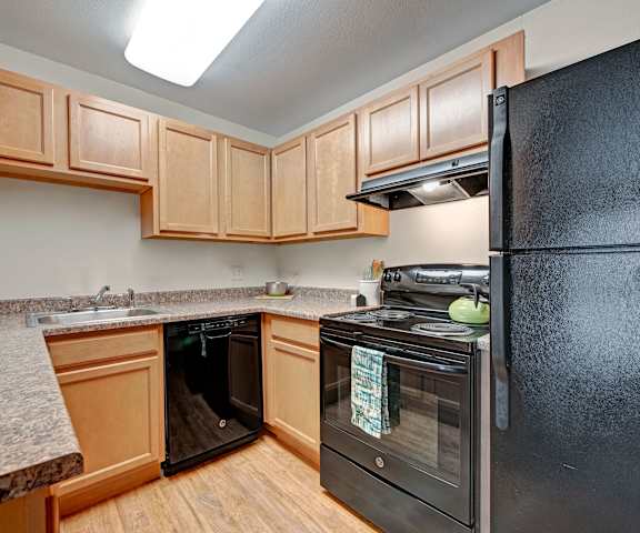 A kitchen with black appliances, marble countertops, and wooden cabinets with decorations at Hyde Park Apartments. 