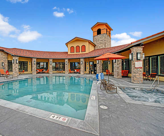 The turquoise outdoor pool with pool chairs, tables, and chairs with the apartments in the background at La Bella Vita Apartments. 