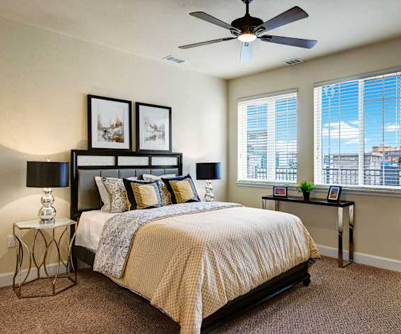 A bedroom with a queen-size bed, fan, a dresser, decorations, window, and nightstands at La Bella Vita Apartments. 