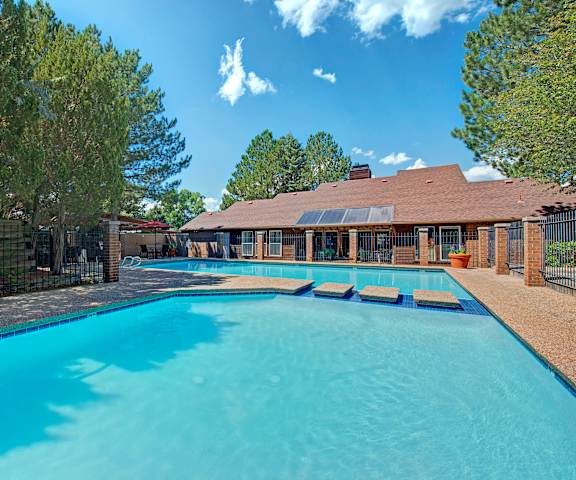 The large, turquoise outdoor pool with pool chairs, tables, and chairs with the apartments in the background at Windtree Apartment Homes. 
