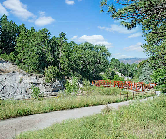Yorkshire Square Cottonwood Creek Trail Entrance The entrance to the Cottonwood Creek Trail at Yorkshire Square Apartment Homes, with an orange bridge over a creek, surrounded by trees and grass.