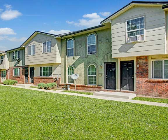Yorkshire Apartments The exterior of the apartments and the green space with grass, trees, and shrubs at Yorkshire Square Apartment Homes.