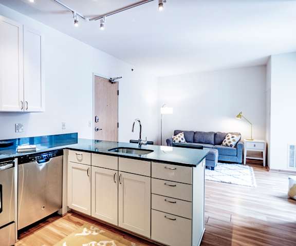 A kitchen with a counter top and a sink and a microwave, with a couch in the background at 7West. 