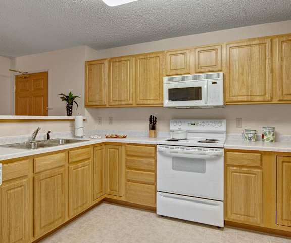 A kitchen with white appliances, light counter, and spacious wooden cabinets at Heritage Park.
