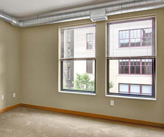 An empty carpeted bedroom with windows at Lofts at Farmers Market Apartments. 