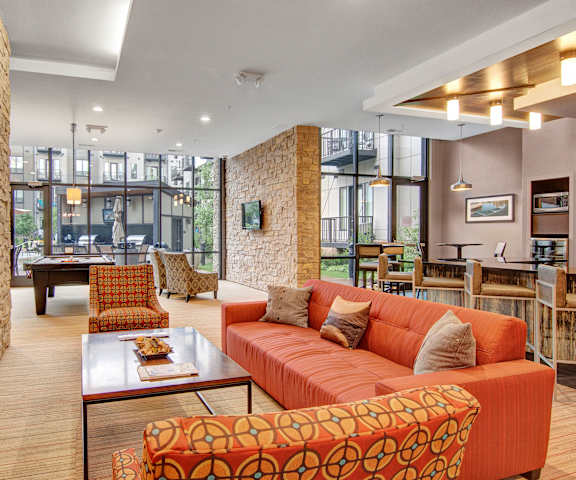A wonderful resident lounge with an orange couch, orange plush chairs, tables, chairs, and a pool table at Residence at the COR Apartment Homes. 