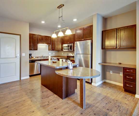 A kitchen with stainless steel appliances and wooden cabinets at Dakota Commons Apartments. 