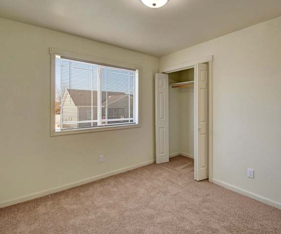 Phoenix Ridge bedroom An empty carpeted bedroom with a closet, window, and overhead lighting at Phoenix Ridge Apartments.