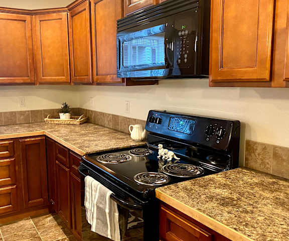 Phoenix Ridge Kitchen The view of the kitchen with marble countertops, a black oven and microwave, large cabinets, and a window at Phoenix Ridge Apartments.