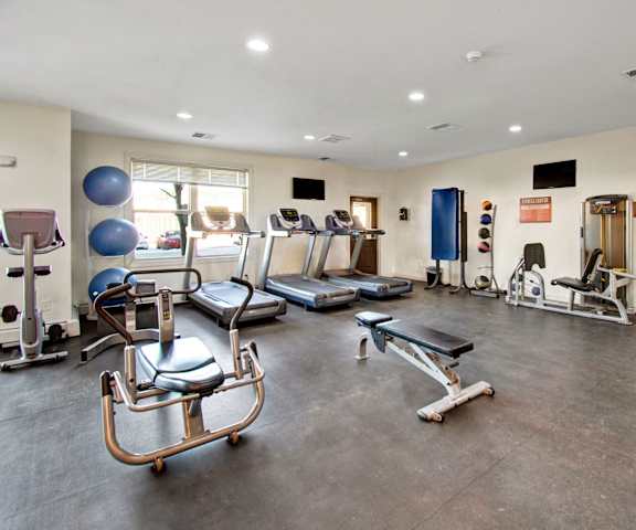 Prairie Pines Gym A gym with cardio machines, windows, TVs, and weights at Prairie Pines at the Ridge Apartment Homes.