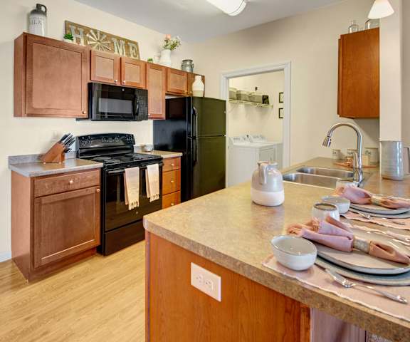 Prairie Pines Kitchen A large kitchen with black appliances, spacious marble countertops, and large wooden cabinets with decorations and appliances at Prairie Pines at the Ridge Apartment Homes.