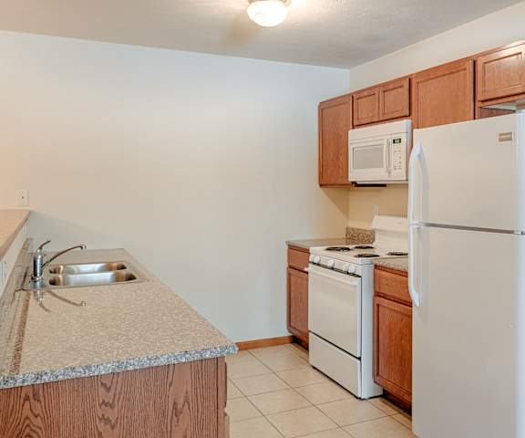 A cozy kitchen with white appliances, overhead lighting, light countertops with lots of room, and large wooden cabinets at Rockridge Apartment Homes. 