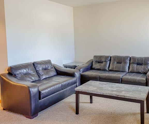 A living room with white walls, three dark marble coffee tables, and two leather couches at Rockridge Apartment Homes. 