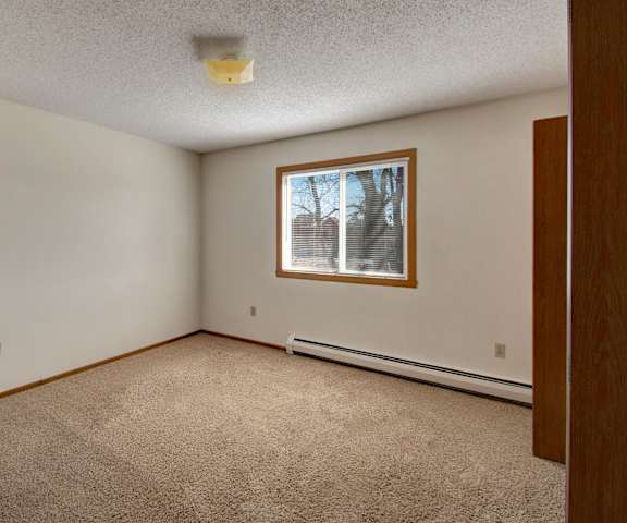 A large, empty carpeted bedroom with overhead lighting and a window at Windscape Apartment Homes. 