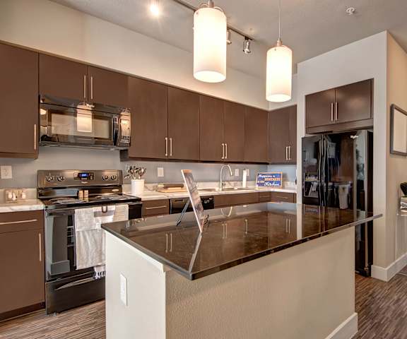 A spacious kitchen with black appliances, a kitchen island with a black countertop, white countertops with lots of room, and black cabinets at the Enclave at Brookside Apartment Homes. 