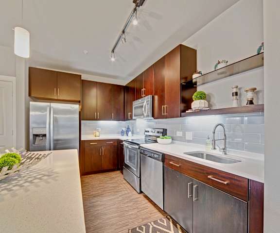 A large kitchen with stainless steel appliances, white marble countertop with ample space, and large wooden cabinets at Metropolitan Apartments. 
