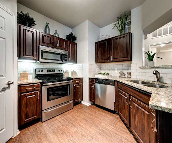 A kitchen with wooden cabinets, stainless steel appliances, and marble countertops at Firestone at West 7th. 