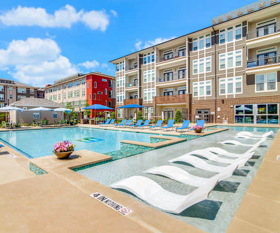 Harmony Luxury Pool The turquoise outdoor pool with pool chairs, tables, and chairs with the apartments in the background at Harmony Luxury Apartments.
