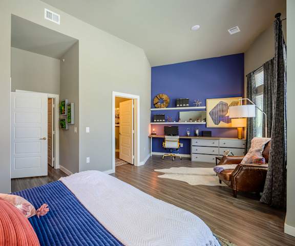 A bedroom with a blue and white queen-size bed, a desk with a computer, decorations, drawers, a window, a closet, and nightstands at Harmony Luxury Apartments. 