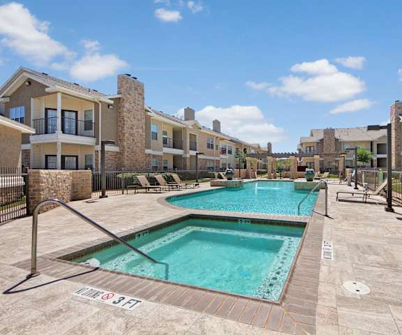 The turquoise outdoor pool with pool chairs, tables, and chairs and the turquoise jacuzzi with the apartments in the background at Mission Green Apartments. 