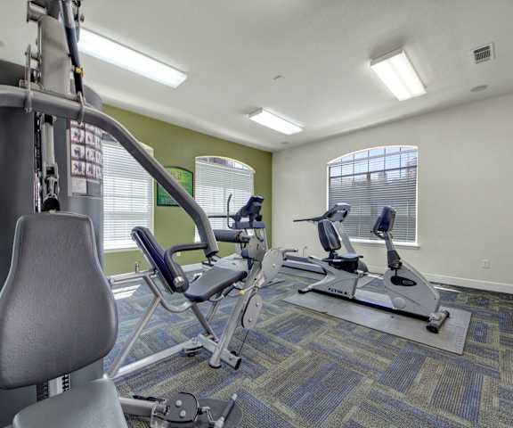 A gym with cardio machines, windows, TVs, and weights at Mission Green Apartments. 