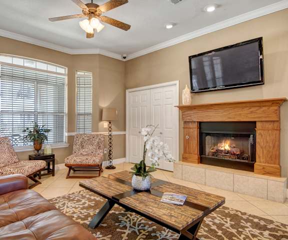 The resident lounge with a fireplace, couches, decorations, large windows, TV, plush chairs, and coffee tables at Mission Green Apartments. 